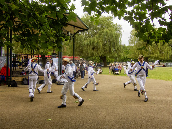 Jockey Morris in their Cotswold Morris costume dancing in a circle in front of the bandstand on the recreation ground